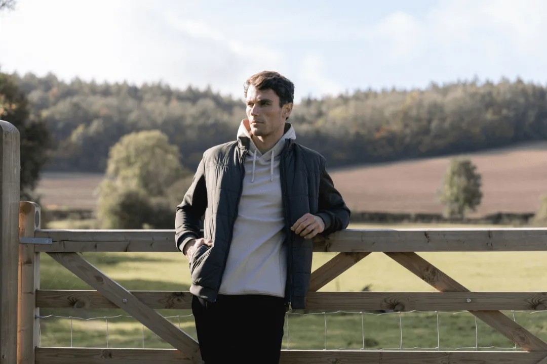 Man in a dark jacket leaning on a wooden gate in the countryside