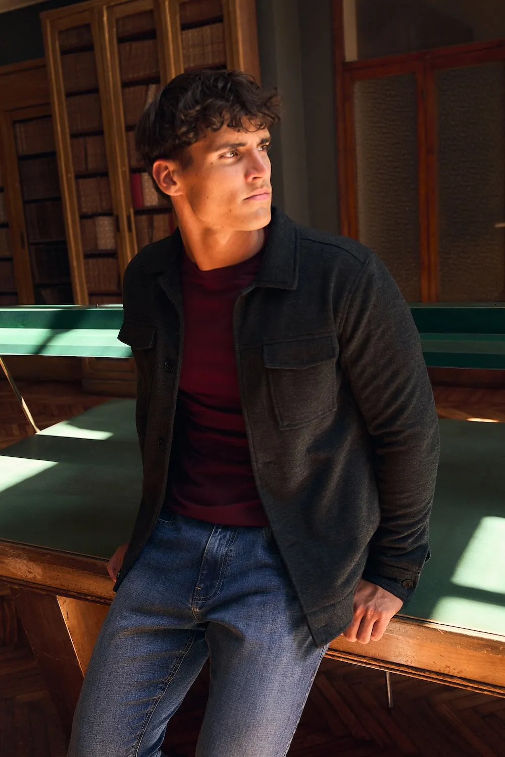 Man in a dark jacket and jeans standing in a wood-panelled library
