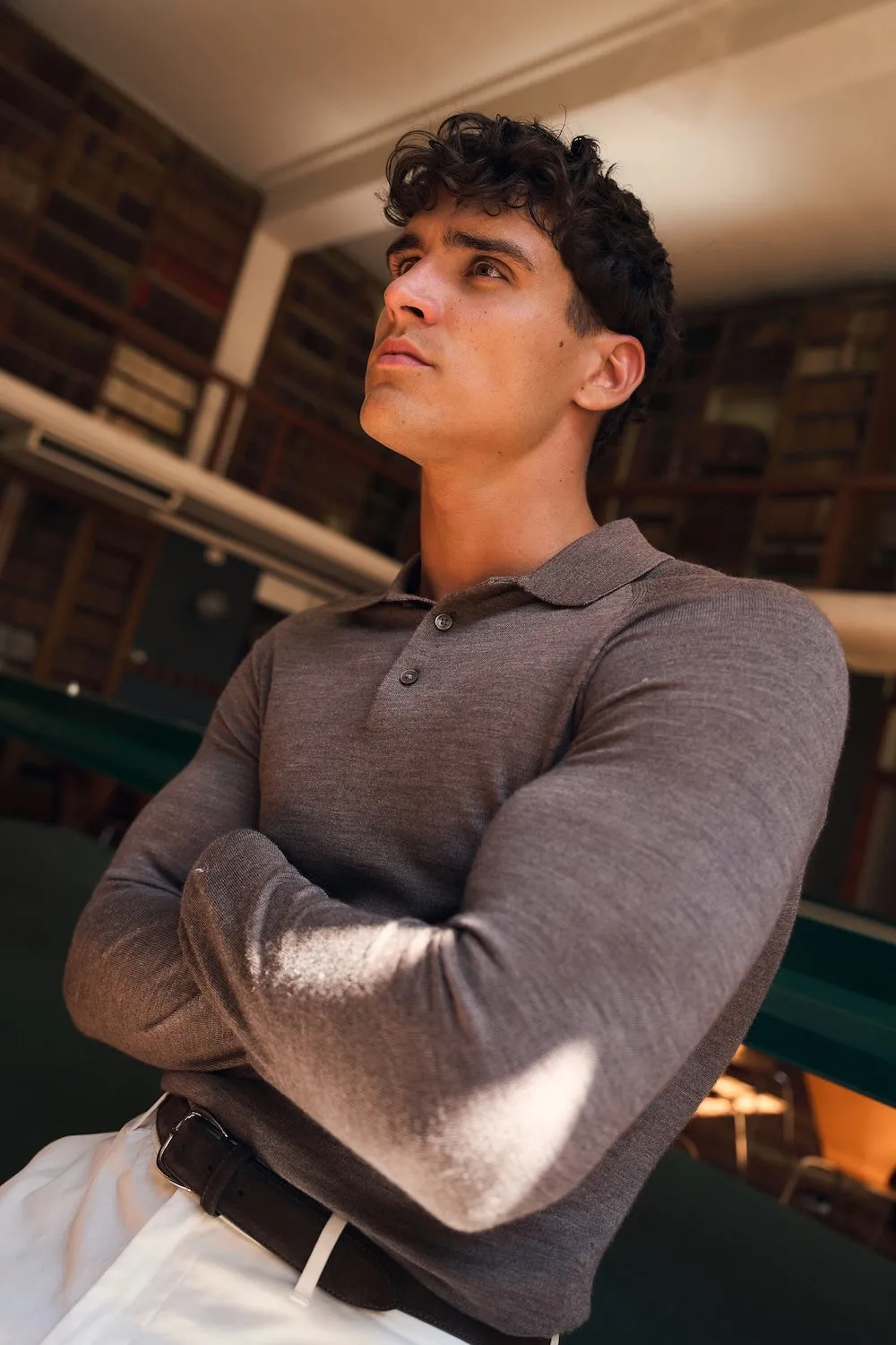 Man in a grey knitted polo with arms crossed, looking up